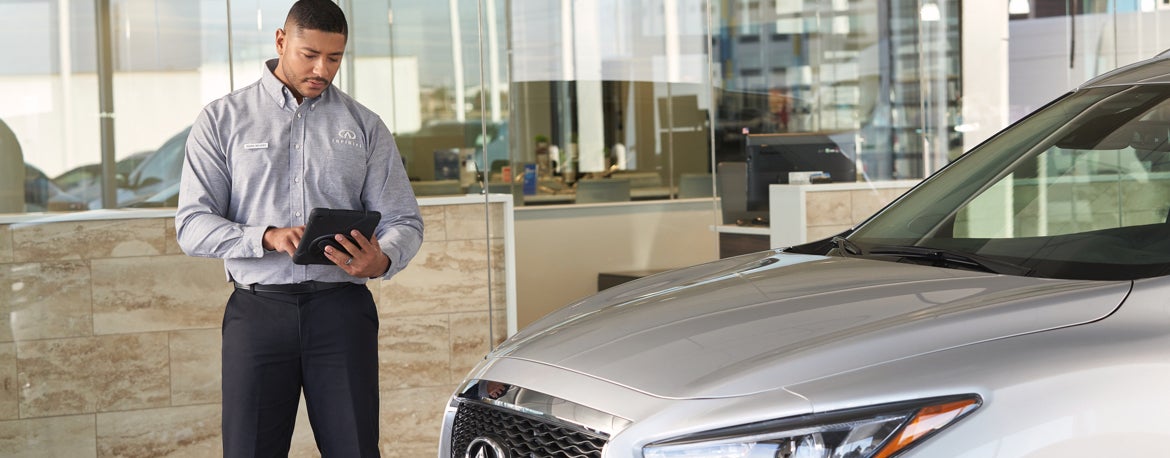 INFINITI Sales associate reviewing vehicle in dealership showroom.
