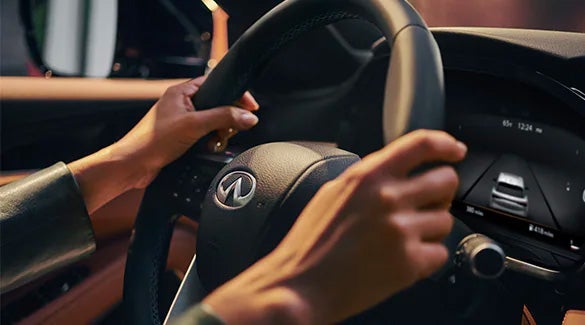 Interior close-up view of a driver's hands on an INFINITI steering wheel