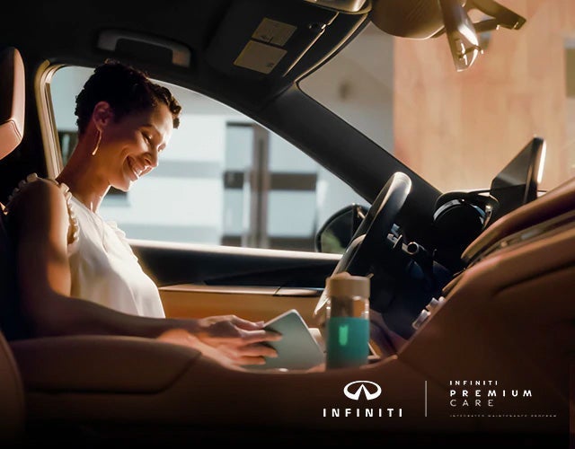 Woman sitting inside her INFINITI vehicle reading her tablet